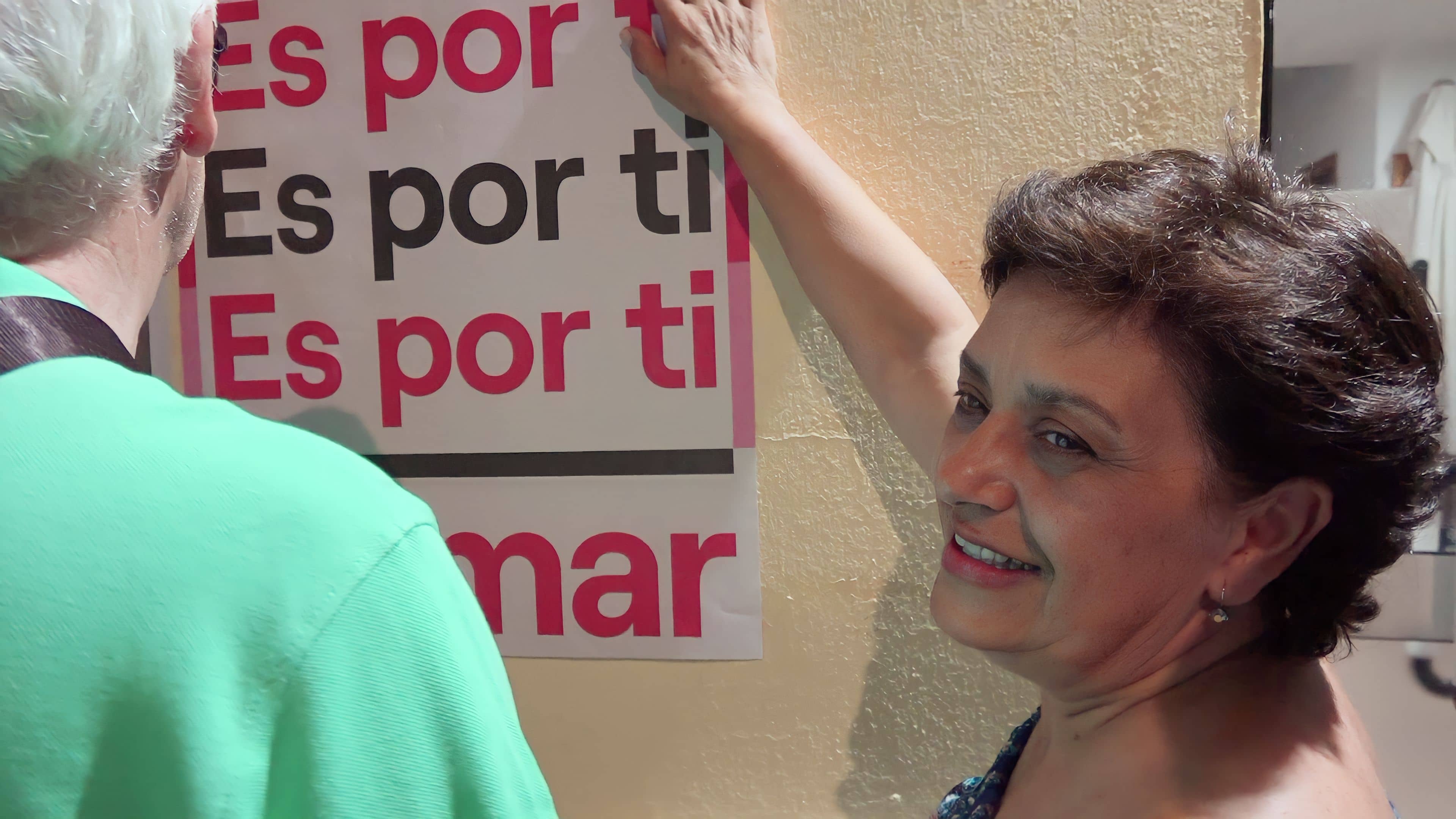 Concepción Rico y Paco Algaba colocan uno de los carteles de campaña en la puerta de la sede de IU El Viso
