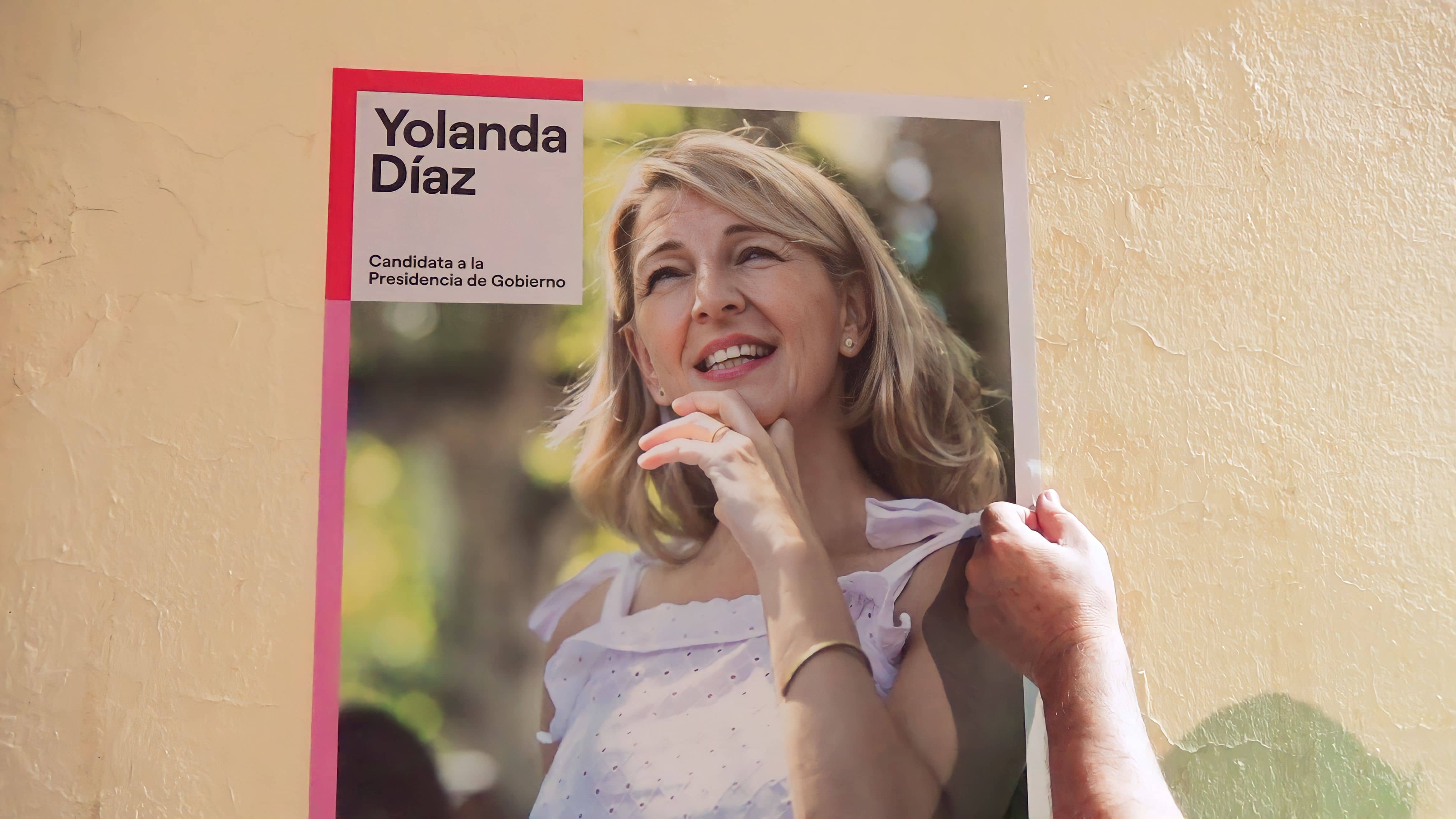 Paco Algaba termina de colocar un cartel electoral de Yolanda Díaz, en la puerta de la sede de IU El Viso.